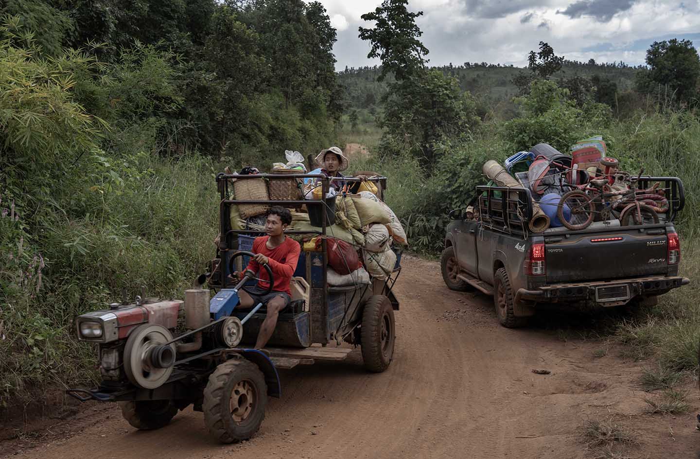 Two trucks loaded with belongings drive down a dirt road