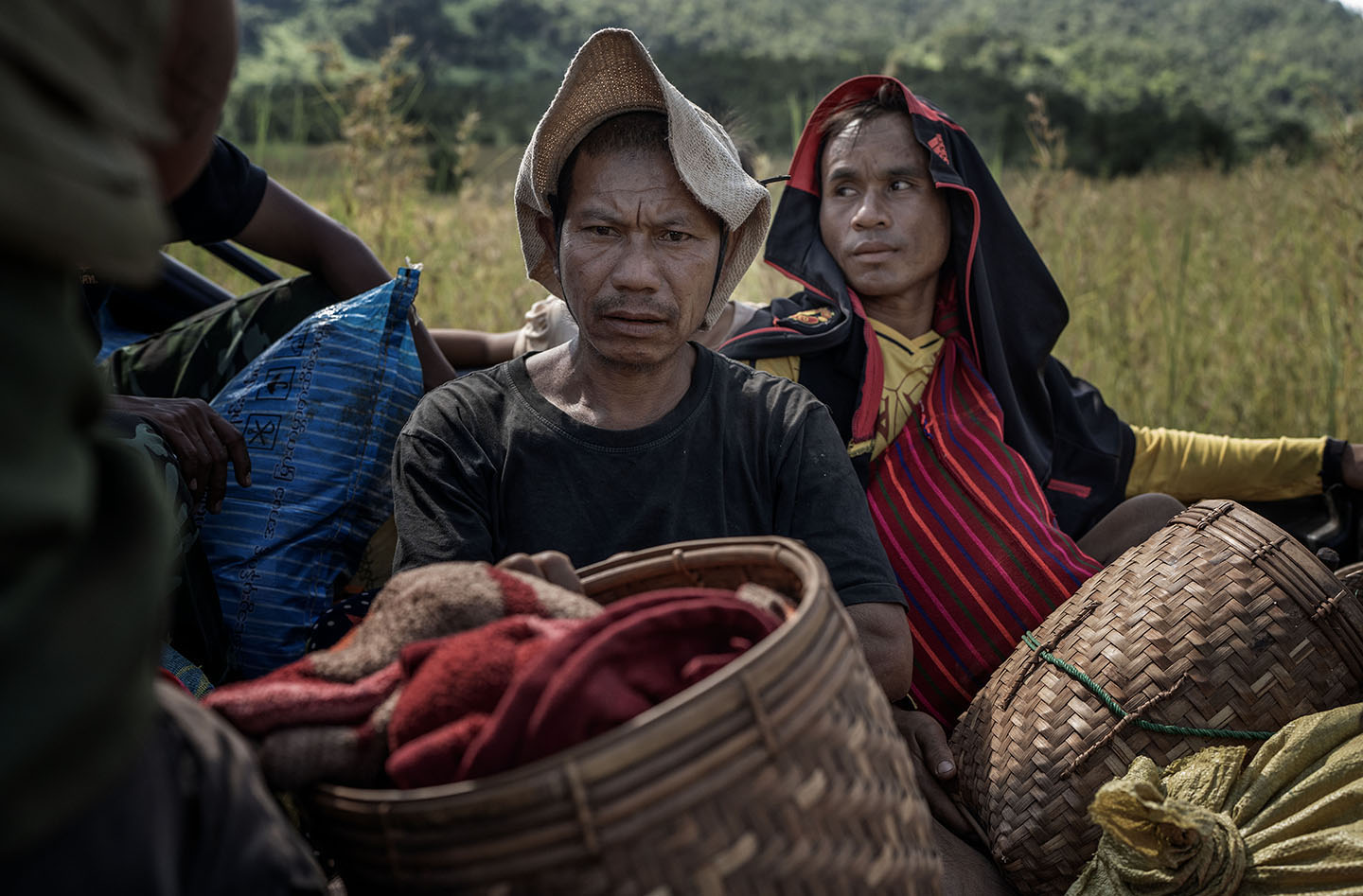 Two men with baskets of belongings cover their heads with a hat and jacket