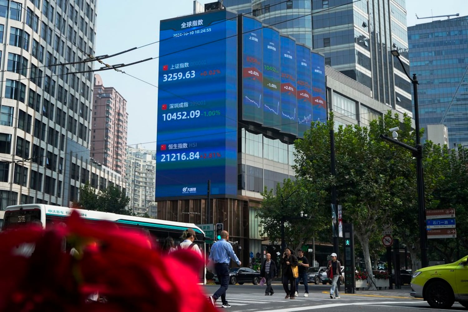 Pedestrians pass by an electronic board displaying Shanghai, top, Shenzhen, center, and Hang Seng, bottom, shares trading indexes at a commercial office building in Shanghai, Oct. 10, 2024. (Andy Wong/AP)